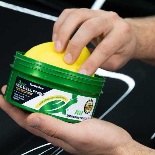 Detailing car? Hands prepare to use Turtle Wax Super Hard Shell Finish Soft Paste Wax with an applicator.