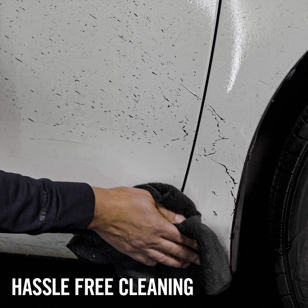 Removing automotive grime. A hand holds a microfiber cloth to clean messy car paint near a tire. Turtle Wax available.