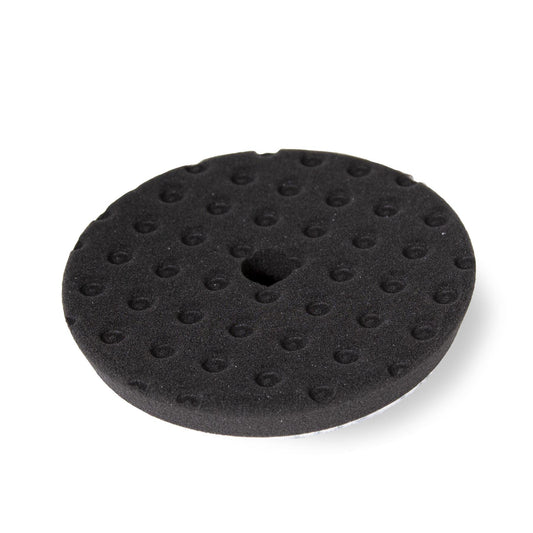 Detailing: Black foam buffing pad. Round, textured surface with center hole. Car care or auto body work supply.