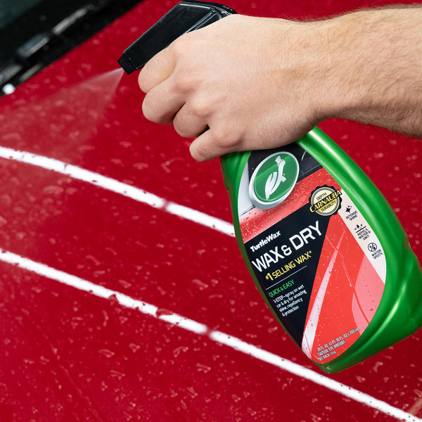 Applying Turtle Wax & Dry spray on a red car's wet surface. The product features carnauba durability for intense shine. US.