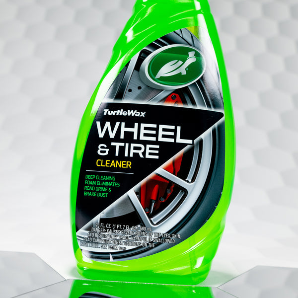 Hero shot of Turtle Wax Wheel and Tire Cleaner bottle standing on a wet floor next to a tire.