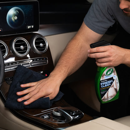 Turtle Wax Fresh Clean All-Surface Cleaner shown as someone wipes down a car's wood-paneled dashboard with a microfiber cloth.