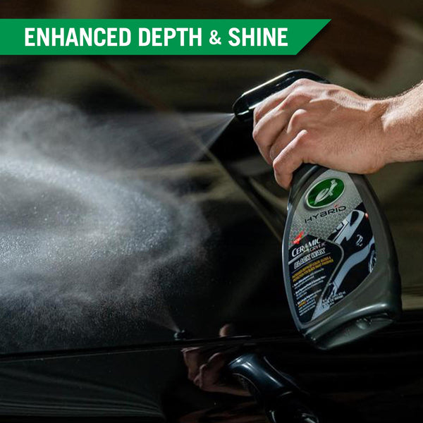 A hand sprays Ceramic Acrylic Black Wax onto the surface of a black car. 