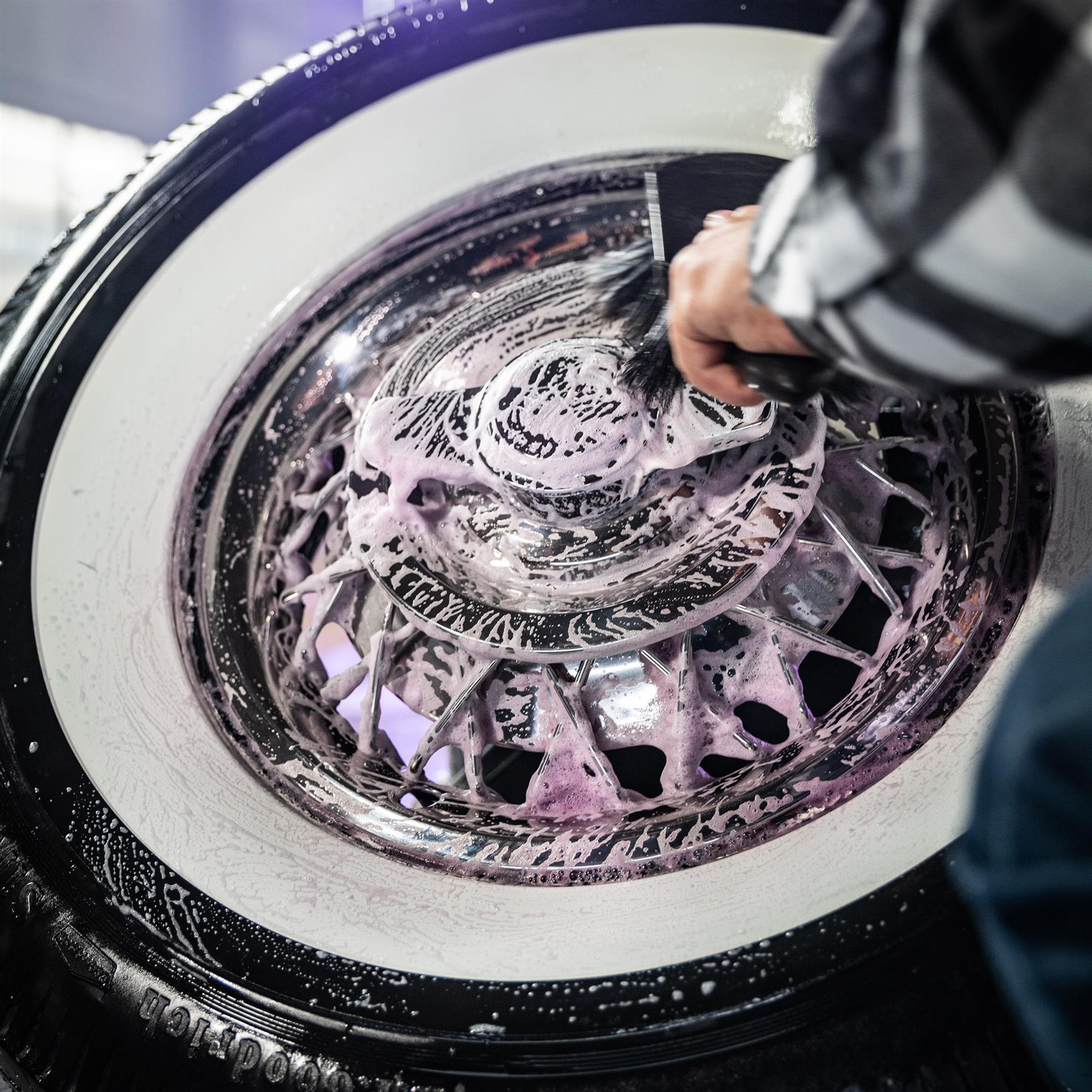 Cleaning classic car wheels. Soap covers rims and whitewall tires during detailing.