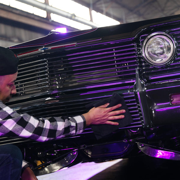 Hand using a microfiber cloth to apply Quick Detailer to a black car door for streak-free shine.