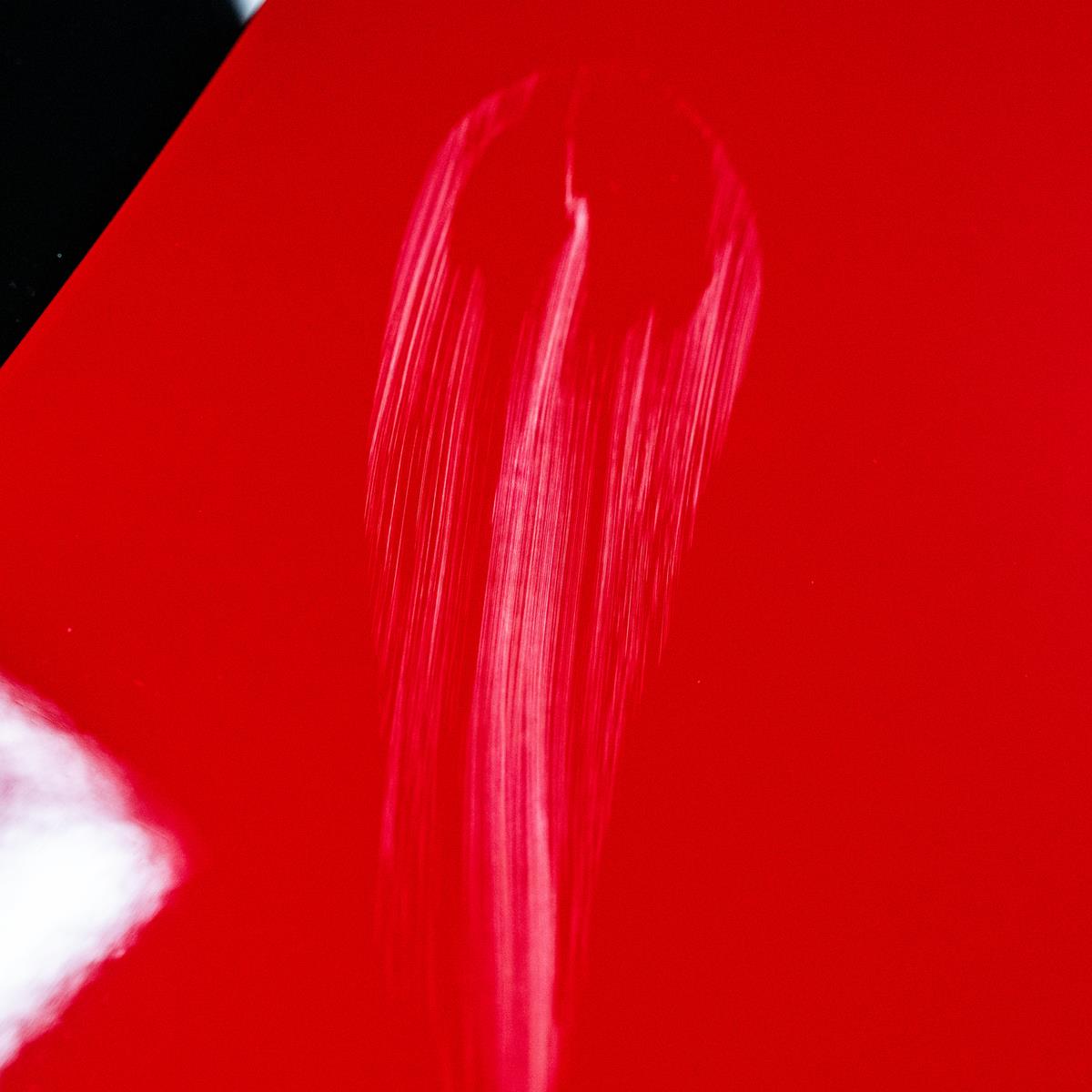 Red car paint shows swirl mark scratches. Automotive detailing or paint correction concept.