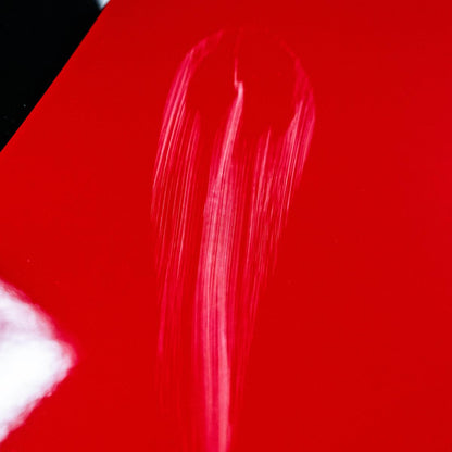 Red car paint shows swirl mark scratches. Automotive detailing or paint correction concept.