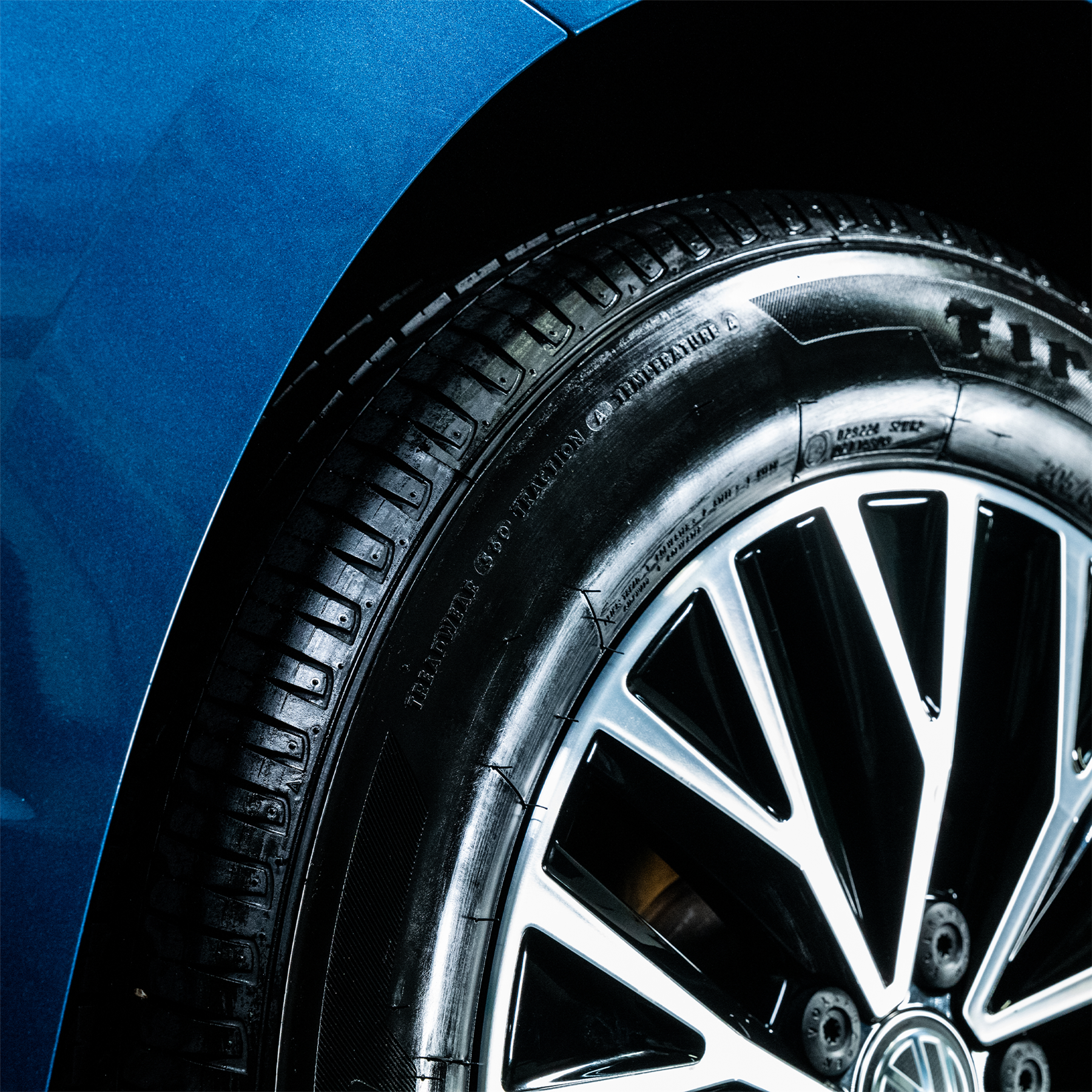 Close-up of a car tire with a glossy, wet look and shiny silver rim against a blue vehicle body. Automotive detailing.