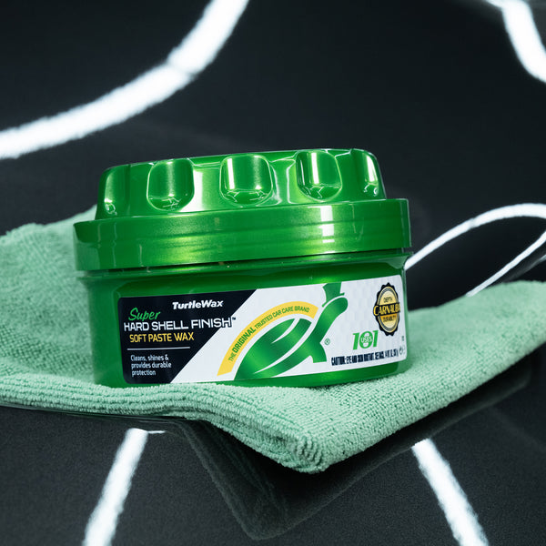 Super hard shell paste wax sits on a green microfibre cloth on the surface of a black car. 
