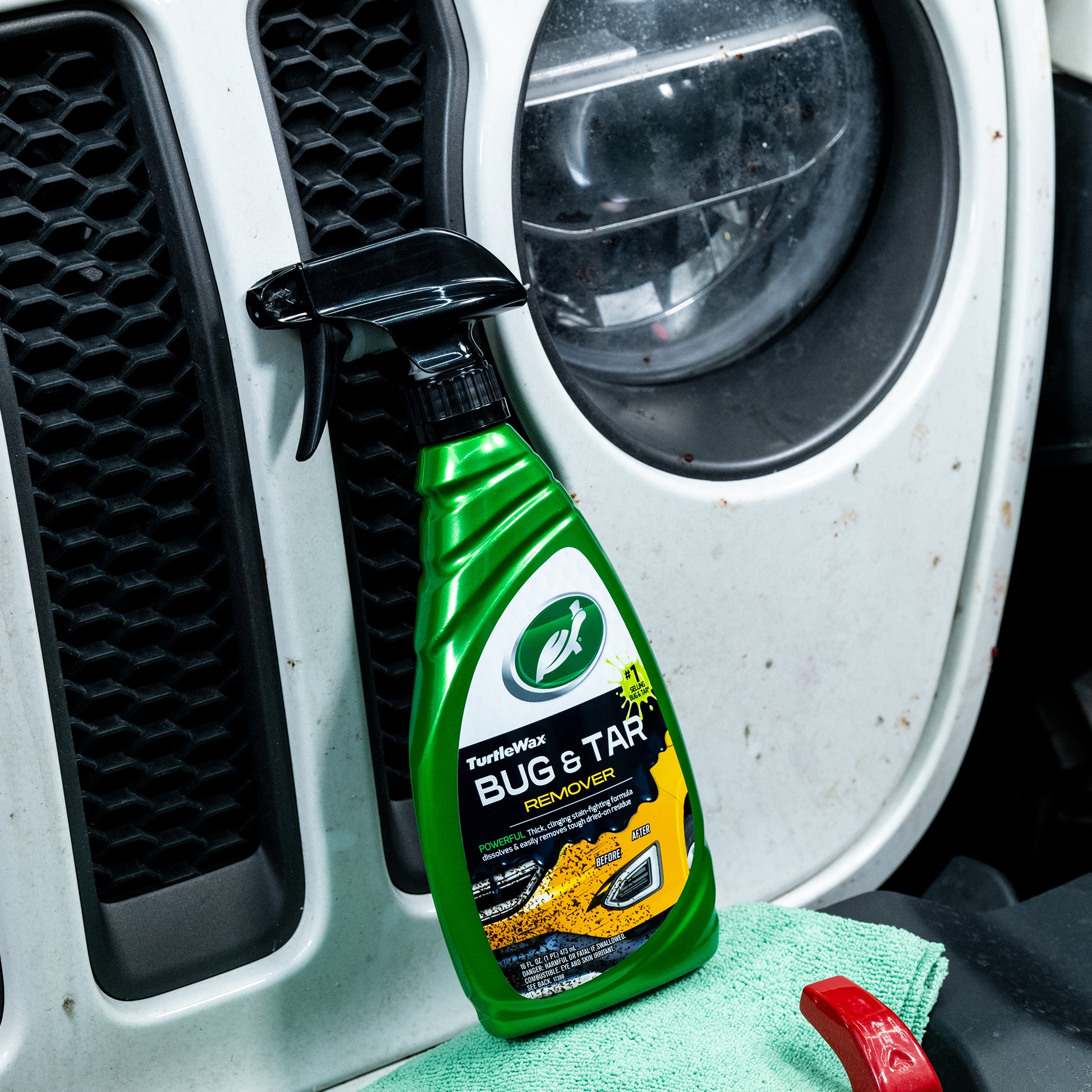 Dirty car grill with headlight and Turtle Wax bug & tar remover. Green bottle with black spray nozzle on a cleaning cloth.