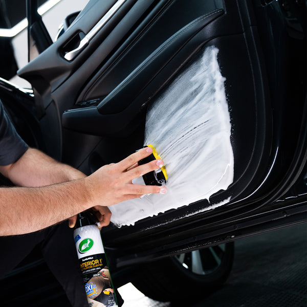 Hand wiping down a car dashboard with a microfiber cloth after applying the cleaner, leaving a clean, streak-free finish.