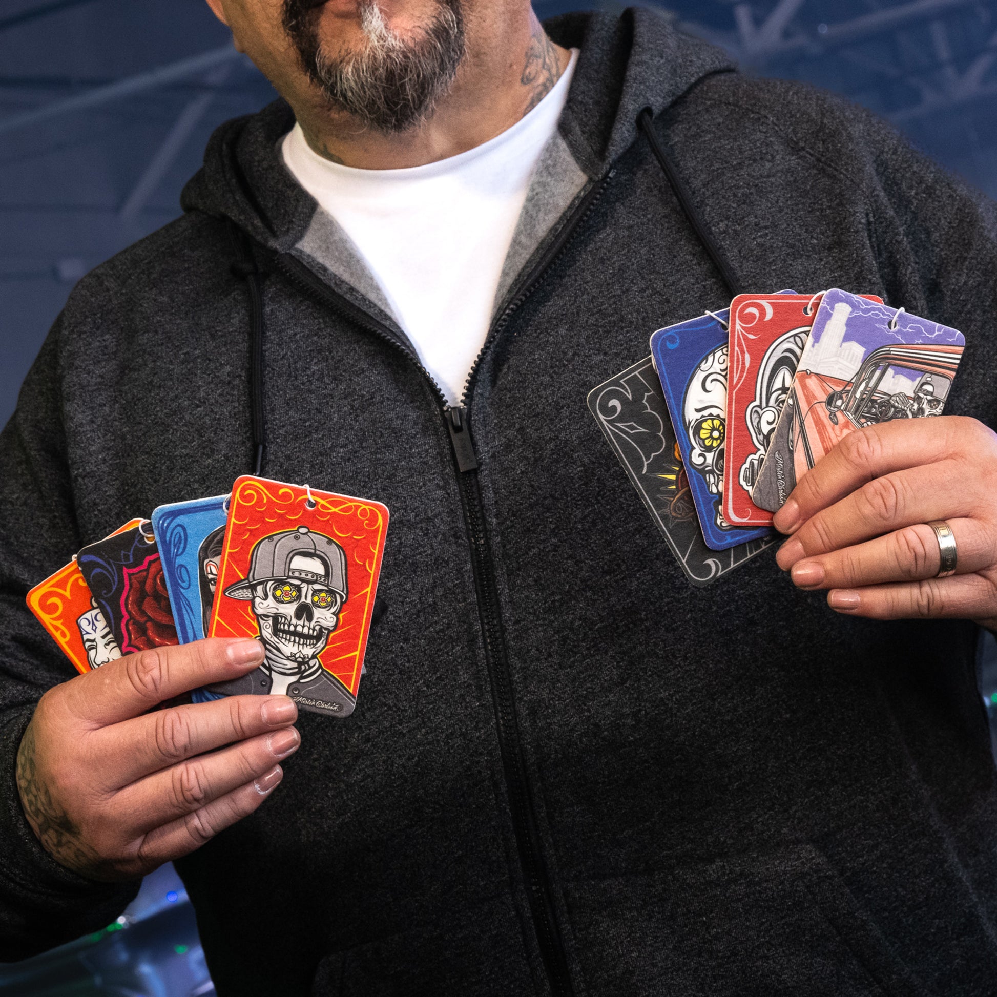Man shows off decorative automotive air fresheners with Day of the Dead & lowrider themes.