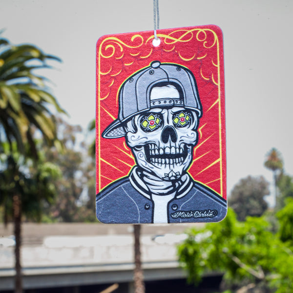 Close-up of Mr. Cartoon Mr. Low-Lo air freshener package laid flat on a textured gray background, with a lowrider design featured prominently.