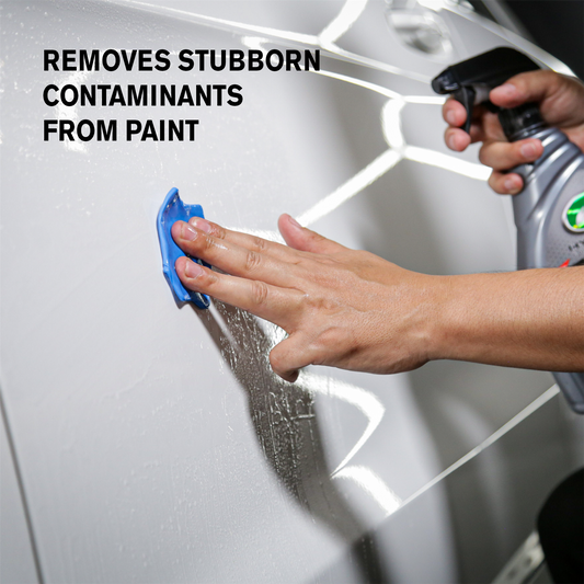 Hand using a blue tool on car paint. Turtle Wax bottle in background. Car detailing for a smooth finish.