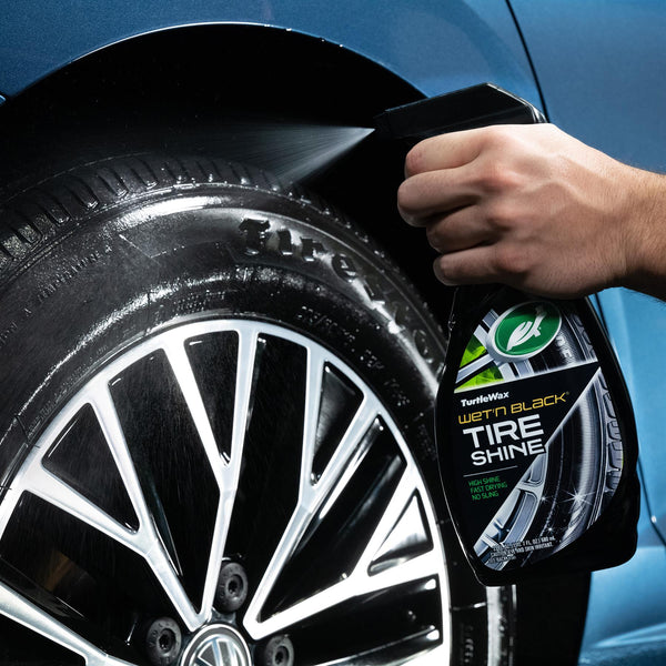 Man in detailing gloves using a polisher on the hood of a shiny black sedan in a garage.