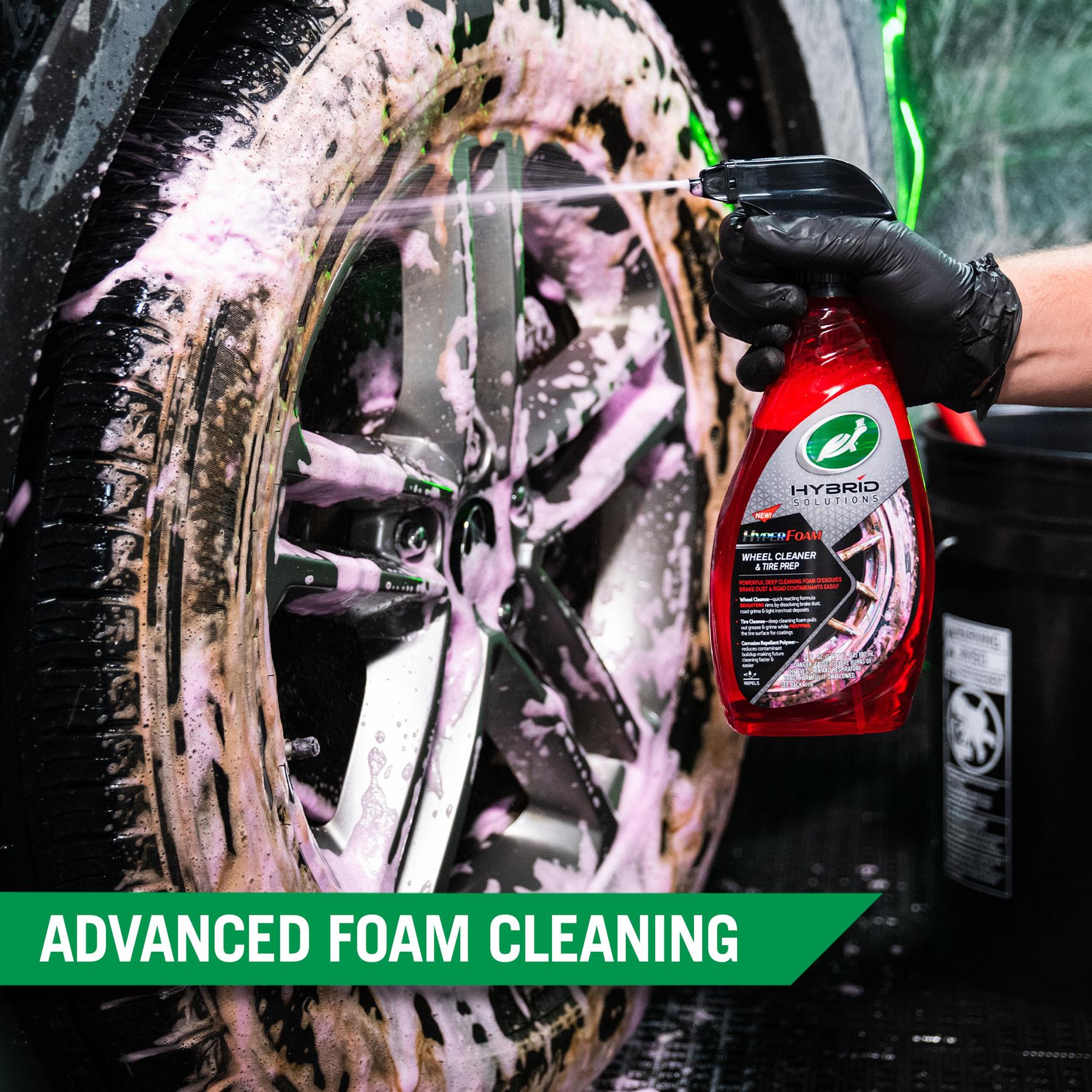 Foam sprays onto a tire and wheel for cleaning. A red spray bottle of Turtle Wax Hyper Foam Wheel Cleaner & Tire Prep is featured.
