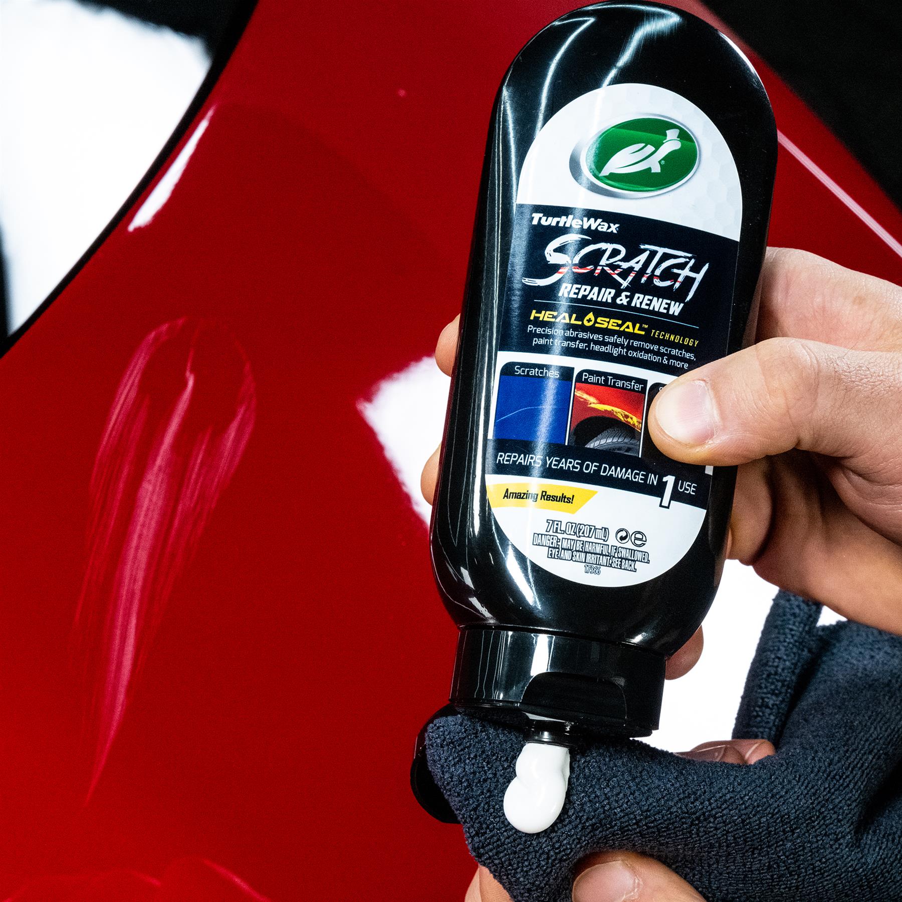 A hand dispenses Turtle Wax Scratch Repair & Renew onto a cloth, near a red car panel. The bottle promises to repair damage.