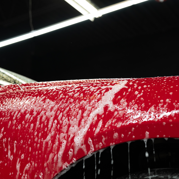 Action shot of Zip Wax Car Wash being rinsed off a vehicle with water spray, showcasing shine and runoff on black paint surface.