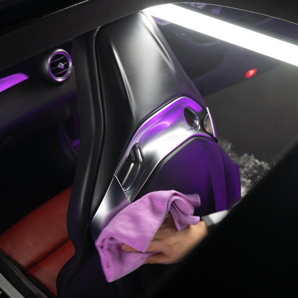 Hand holding Mr. Cartoon Leather, Vinyl & Plastic Cleaner bottle with product being sprayed onto a glossy dashboard surface.