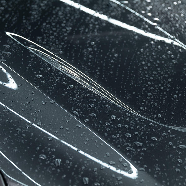 Spraying detailing product across vehicle's paint surface with fine mist.