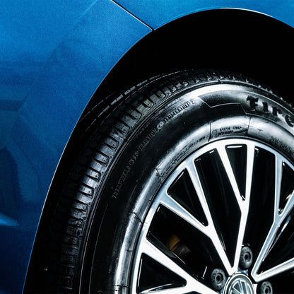 Close-up of a clean car wheel & tire with a blue auto body. Silver and black rims. Black tire tread with glossy tire shine.