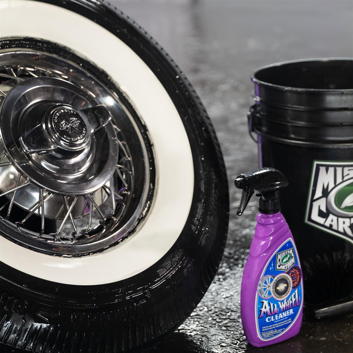 Shiny chrome Chevrolet hubcap on whitewall tire. Turtle Wax Mister Cartoon purple spray bottle and wash bucket. Auto detailing scene.