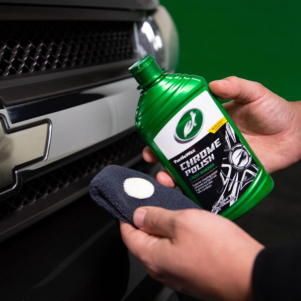 Chrome Polish by Turtle Wax on car. Hands hold bottle and cloth with cream. Removes rust. Cleans auto metal. Car detailing product.