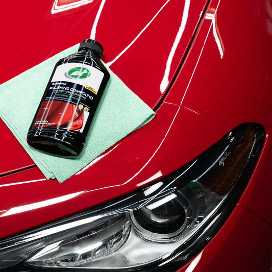 Turtle Wax Polishing Compound & microfiber cloth rest on the red car hood near the headlight. Clean Finish Technology.