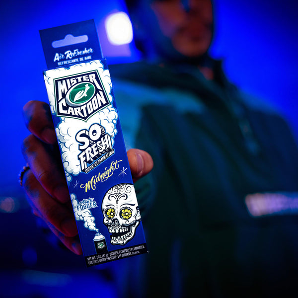 Close-up of a Mr. Cartoon spray can held by a person wearing rings, suggesting urban street style.