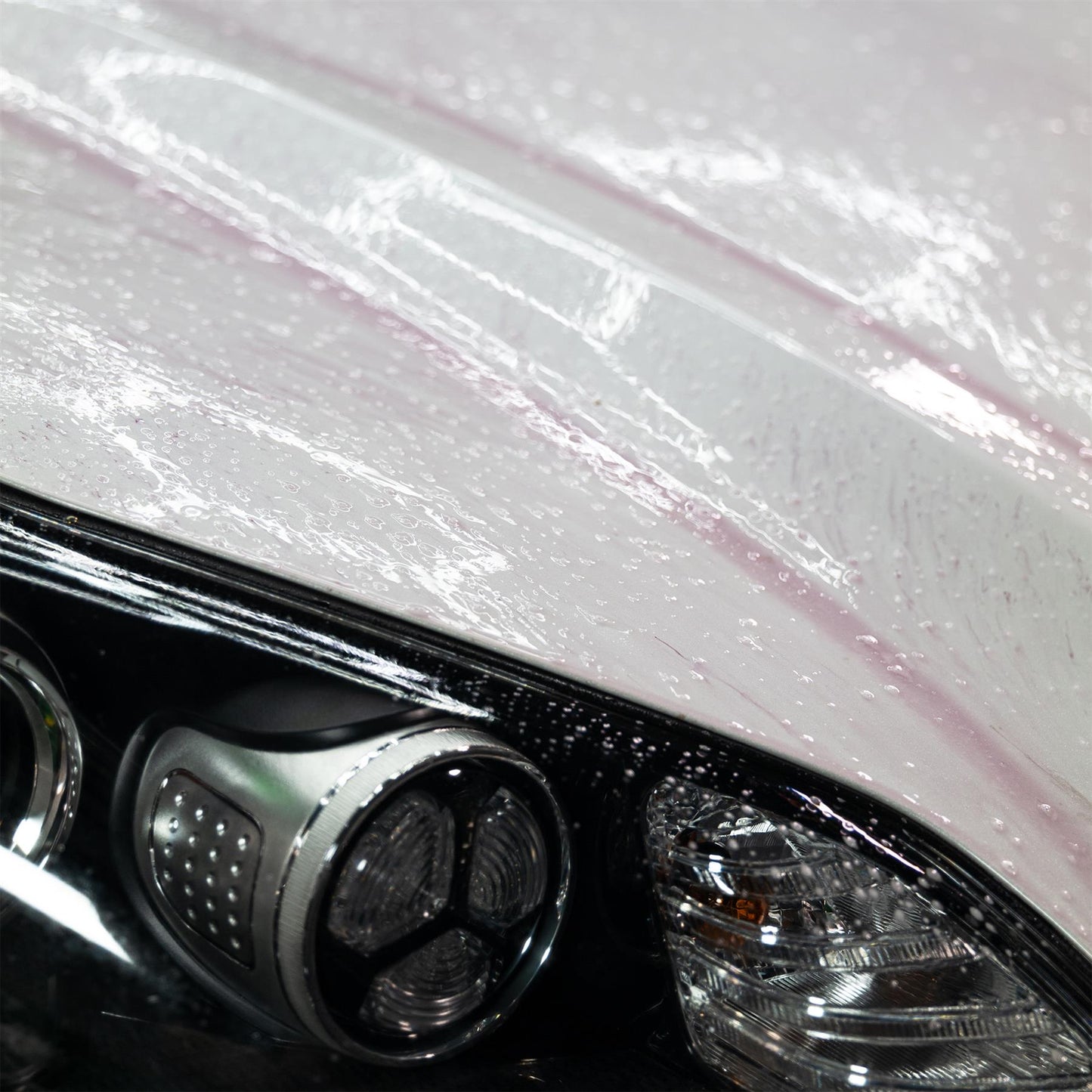 Car detailing. Vehicle cleaning close-up showing water beading on paint and auto headlight.