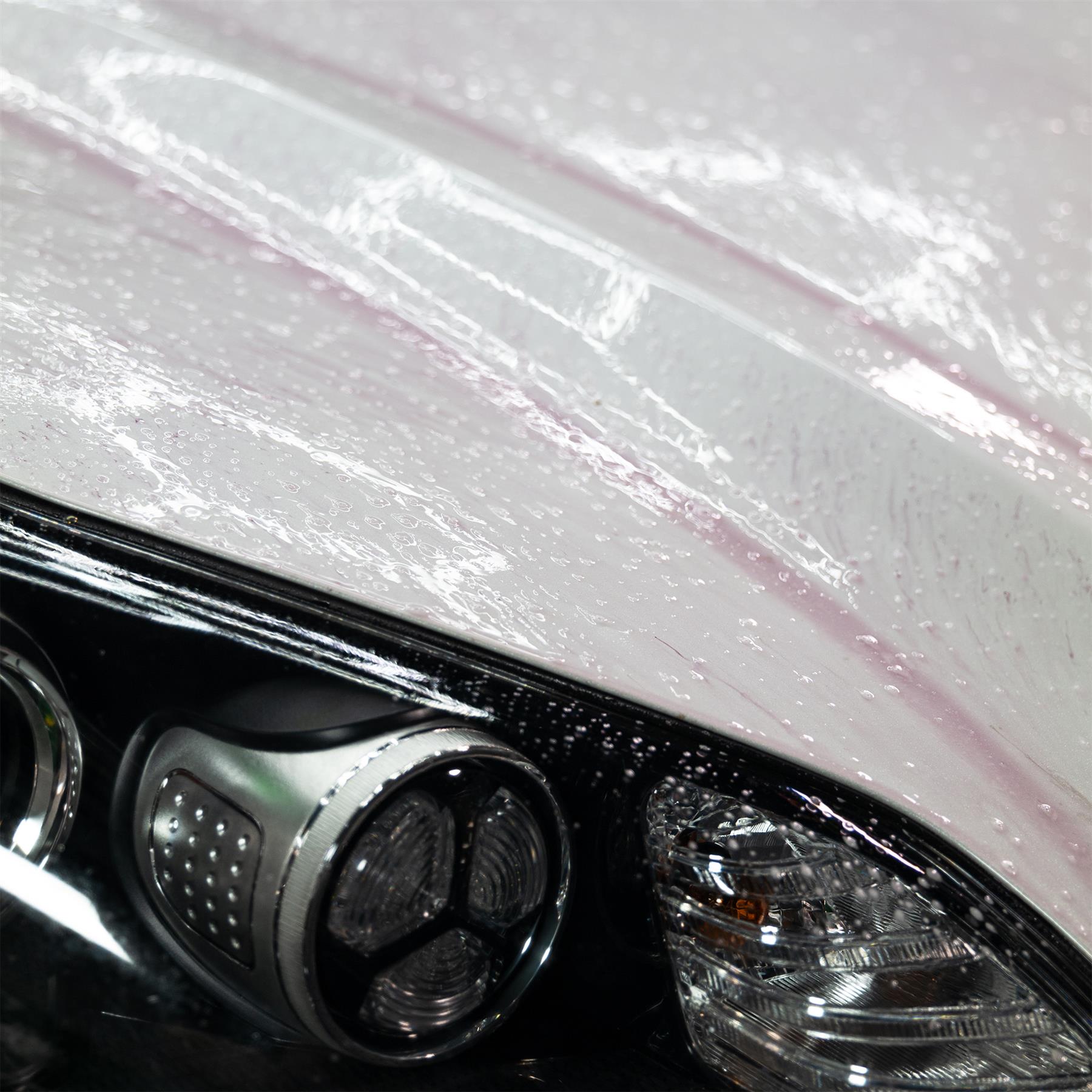 Car detailing. Vehicle cleaning close-up showing water beading on paint and auto headlight.