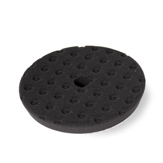 Black foam buffing pad with circular depressions and center hole, used in auto detailing.